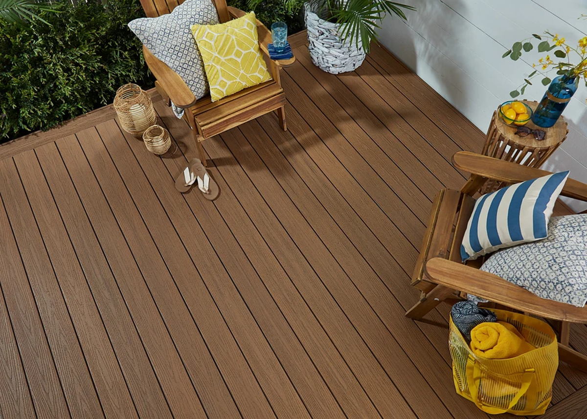A dark chocolate-brown Fiberon deck with Adirondack chairs, patterned cushions and potted greenery against a white wall