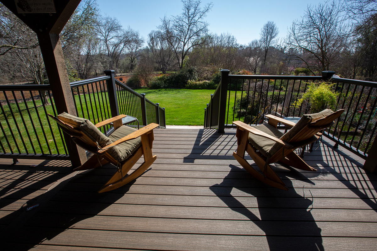 Two wooden rocking chairs on a dark composite deck with black metal railing overlooking a green lawn