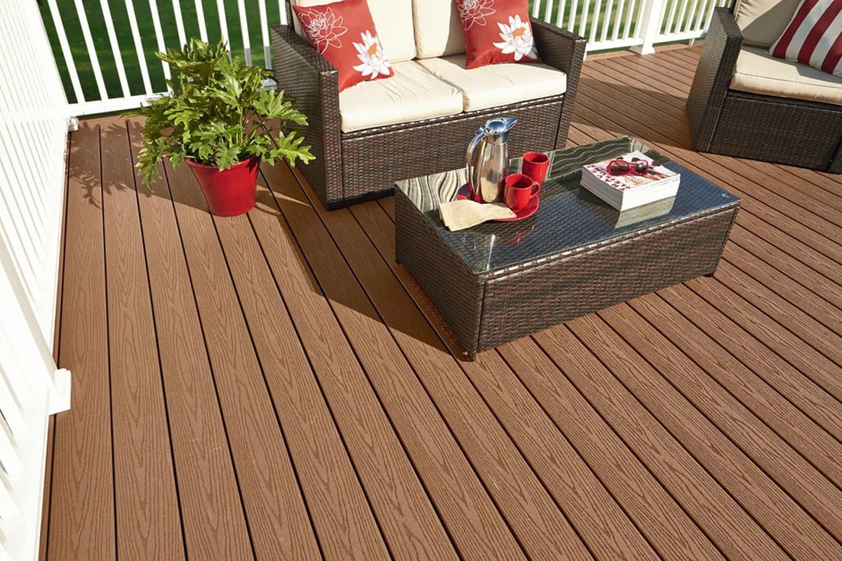 A warm brown Fiberon deck with a wicker sofa set, glass-topped table and white railing, potted plants alongside